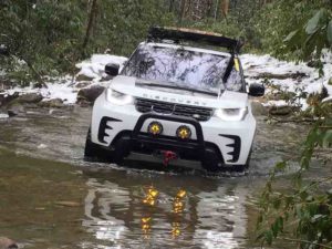 Land Rover Discovery going through a water crossing while off-road in the forest